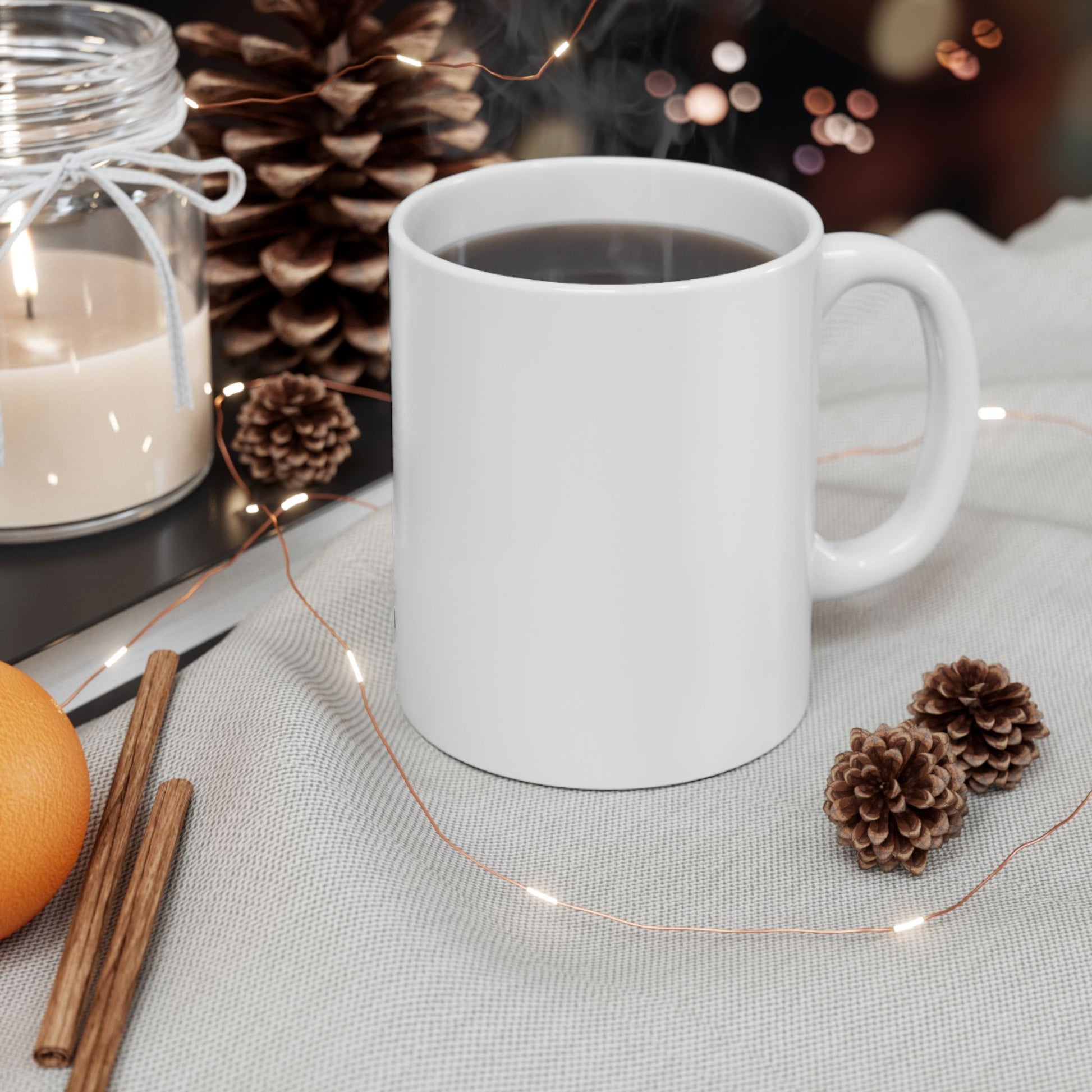 White mug with hot chocolate, surrounded by decorative elements like a candle, cinnamon sticks, and pine cones on a table.