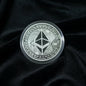 Hand holding a silver Ethereum coin against a velvet surface