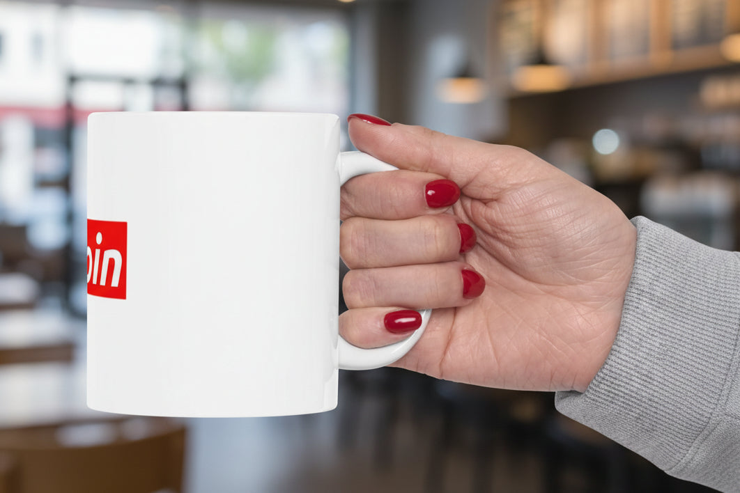 Hand holding a white mug with a red logo on a white background