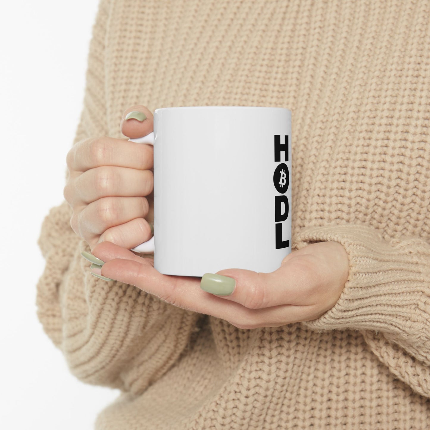Person holding a white mug with 'HODL' printed on it, wearing a beige sweater.
