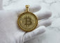Gold Bitcoin pendant held by a gloved hand against a marble background