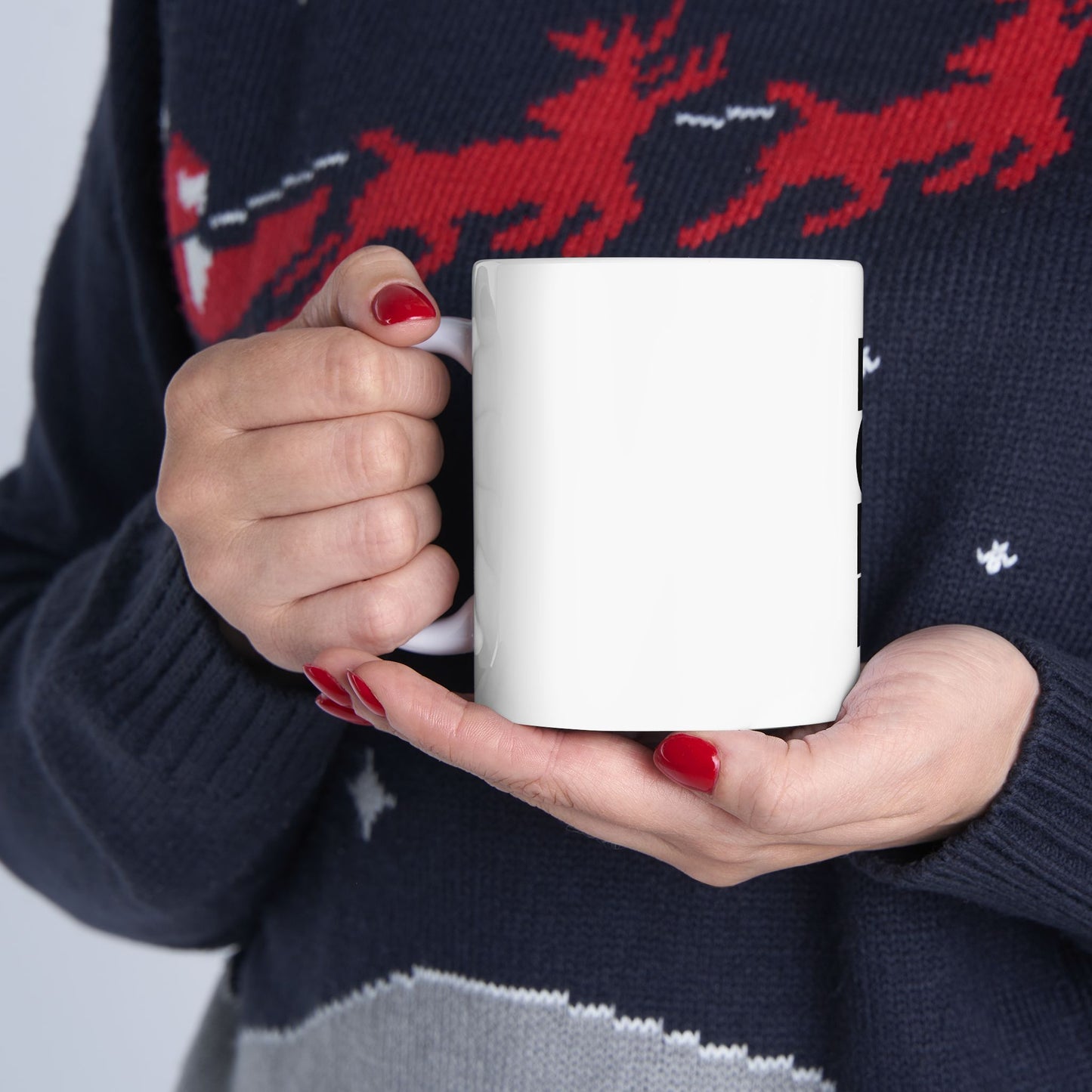 Person wearing a navy sweater with red reindeer holding a white mug.