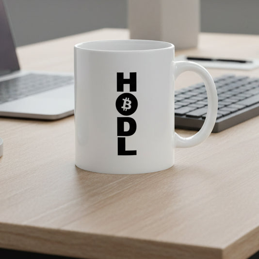 White mug with 'HODL' text on a desk with a laptop and keyboard.