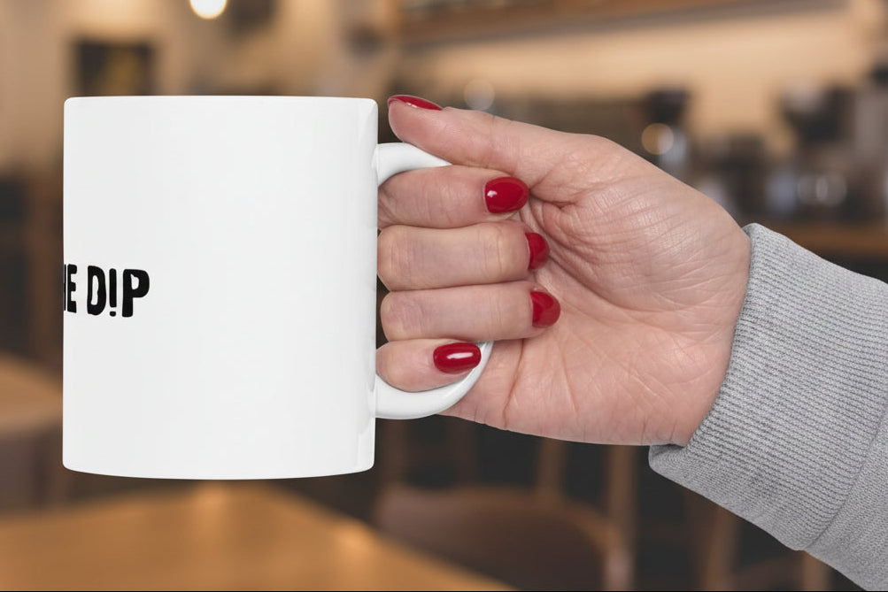 Hand holding a white mug with 'THE DIP' text on a white background