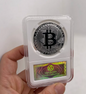 Silver Bitcoin coin in a protective case held by a hand on a white background